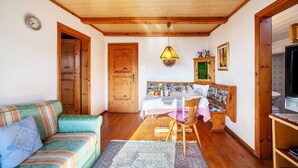 Una sala de estar acogedora con techo de madera, una mesa de comedor con mantel blanco, un sofá y una televisión.