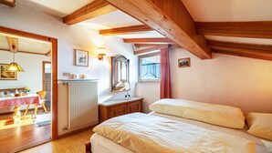 Un dormitorio con techo de madera, una cama, un aparador, un espejo y una ventana con cortinas.