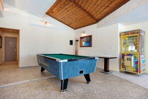 A pool table in a room with a wooden ceiling, a claw machine, and a framed picture on the wall.