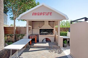 An outdoor barbecue area with a 'PARADISE' sign, a stone fireplace, and a table.
