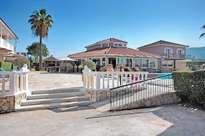 Une maison à deux étages dotée d’un balcon, d’une piscine et d’un escalier en pierre menant à l’entrée.
