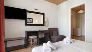 Habitación de hotel con una cama, un escritorio, una silla, un espejo, un teléfono y una puerta que da a otra habitación.