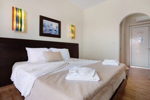 A hotel room with a bed, white linens, a headboard, a painting, and a door. - Paradise Zante Superior Studio 3 with Shared Pool & Wi-Fi (Zakynthos)