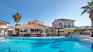 Une piscine dont le fond est décoré de motifs géométriques en mosaïque, un espace extérieur aménagé avec un toit, et un bâtiment doté d’un balcon.