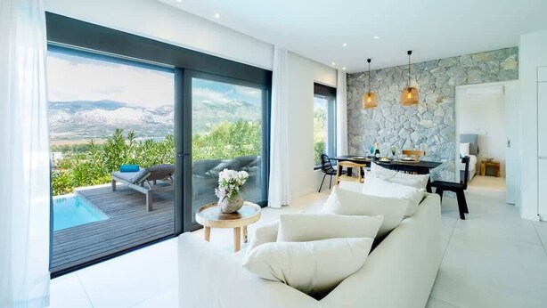 Una sala de estar moderna con un gran ventanal corredera que da a un balcón con piscina. Hay un sofá, una mesa de comedor y luces colgantes.