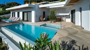 Una casa moderna con piscina, mobiliario exterior y zona de barbacoa.