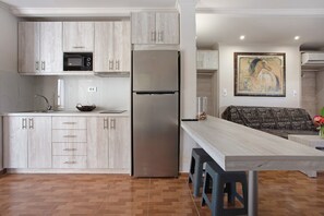 Une cuisine moderne avec des meubles en bois, un réfrigérateur en acier inoxydable, un four à micro-ondes et un coin repas équipé d’une banquette.