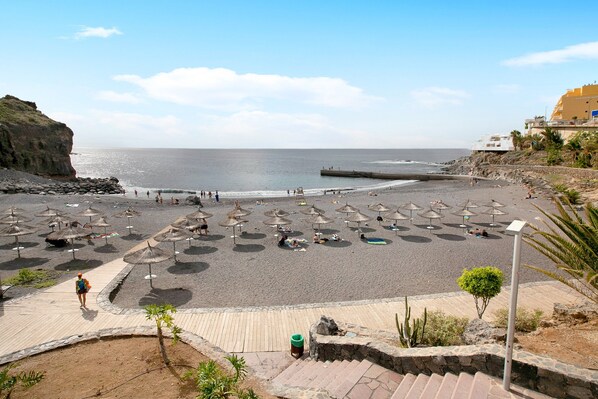A beach with umbrellas, a pier, and a rocky cliff.
