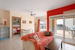 A room with a bed, a desk, a chair, a ceiling fan, and a sliding glass door leading to an outdoor area.