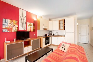 A compact living space with a kitchenette, a television, a sofa, and artwork on the walls.