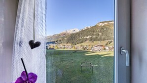 A window view of a grassy field with a small structure, a mountain in the background, and a door frame. - Holiday Apartment "Ciasa Tach" with Mountain View, Balcony & Wi-Fi (Pozza di Fassa)