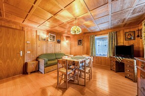 Un intérieur en bois comprenant un canapé, une table à manger, des chaises, un téléviseur et une commode.