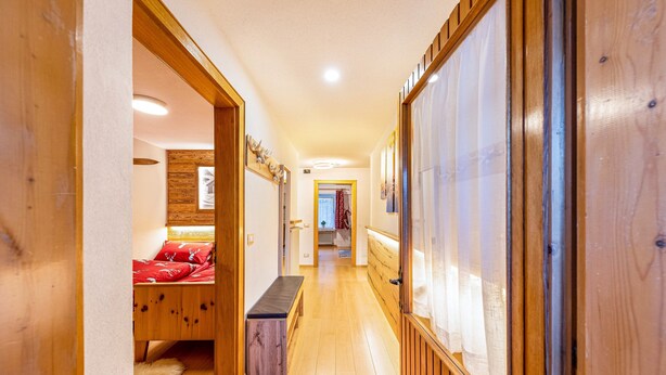 A wooden hallway with a bed, a bench, and a view into another room. - Holiday Apartment "Ciasa Tach" with Mountain View, Balcony & Wi-Fi (Pozza di Fassa)