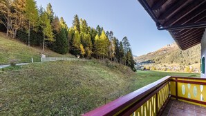 A balcony with a view of a grassy hill, trees, and a distant village. - Holiday Apartment "Ciasa Tach" with Mountain View, Balcony & Wi-Fi (Pozza di Fassa)