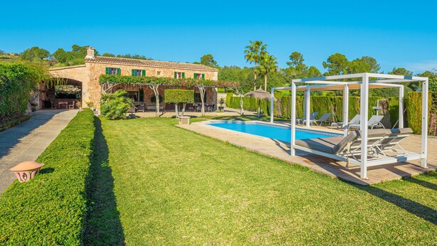 Ein Pool mit Liegestühlen, ein Gebäude aus Stein mit einer überdachten Terrasse und einem gepflegten Rasen.