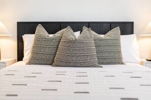 Un llit amb un capçal fosc, roba de llit blanca i almoades amb ratlles.