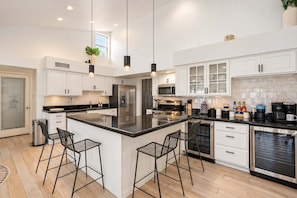 A modern kitchen with white cabinetry, a large island with bar stools, stainless steel appliances, and pendant lighting. - Desert Playground |Pool|Sportcourt |Bocce | Cabana (Scottsdale)