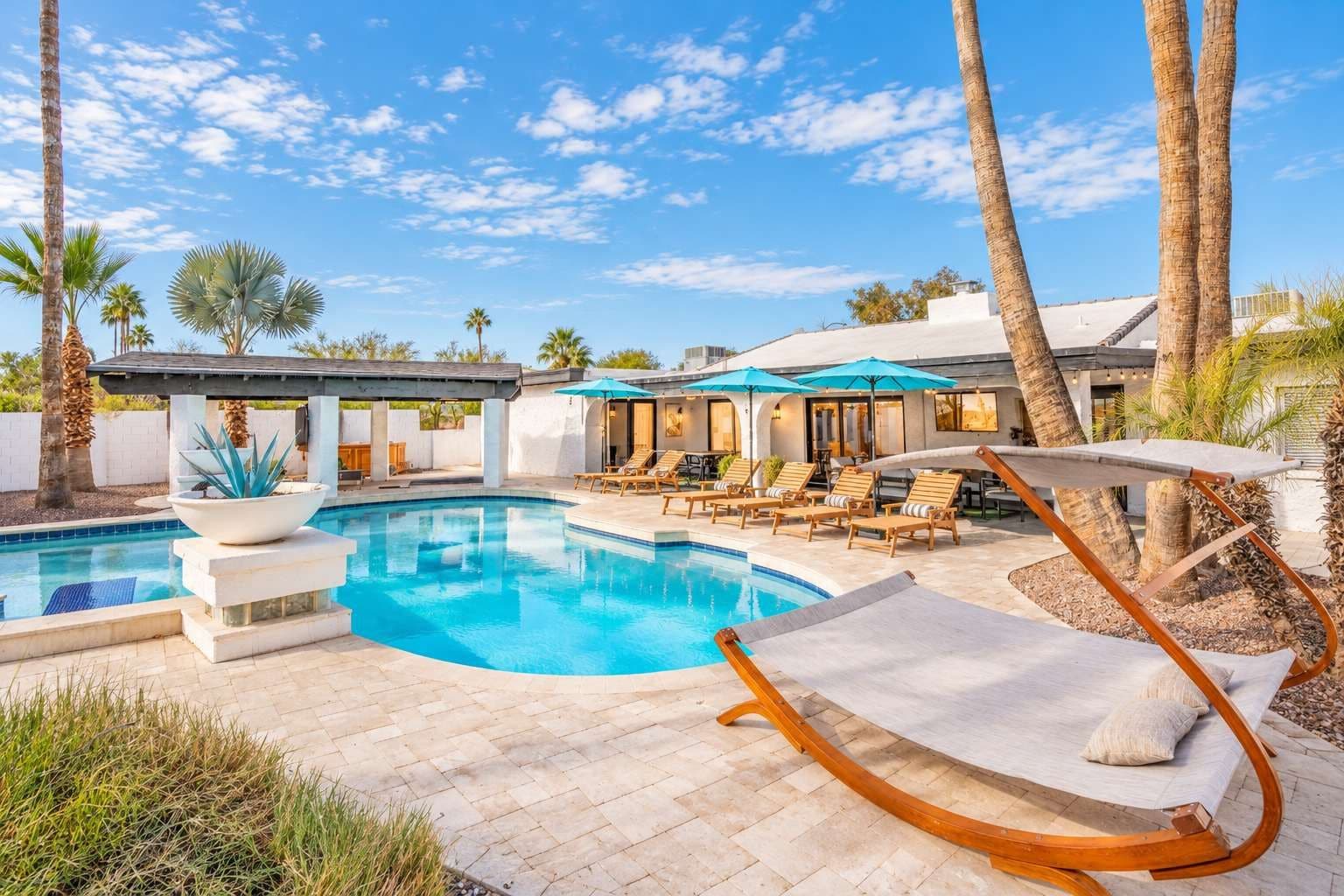 A pool area with lounge chairs, a pergola, and palm trees.