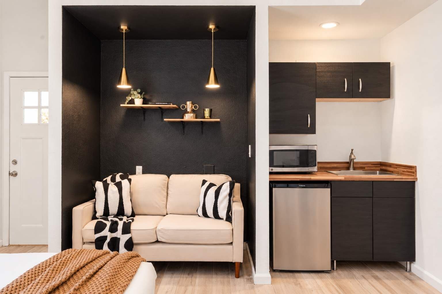 A loveseat sits under two gold pendant lights, right next to a kitchenette with a mini fridge, microwave, and sink, all inside the casita.