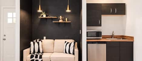 A loveseat sits under two gold pendant lights, right next to a kitchenette with a mini fridge, microwave, and sink, all inside the casita.
