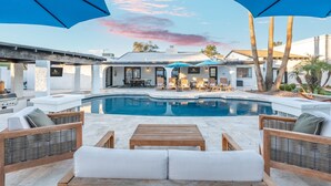 A poolside area with lounge chairs, umbrellas, and a view of a house with a pool. - Desert Playground | Pool, Gym, Bocce & Pickleball. (Scottsdale)