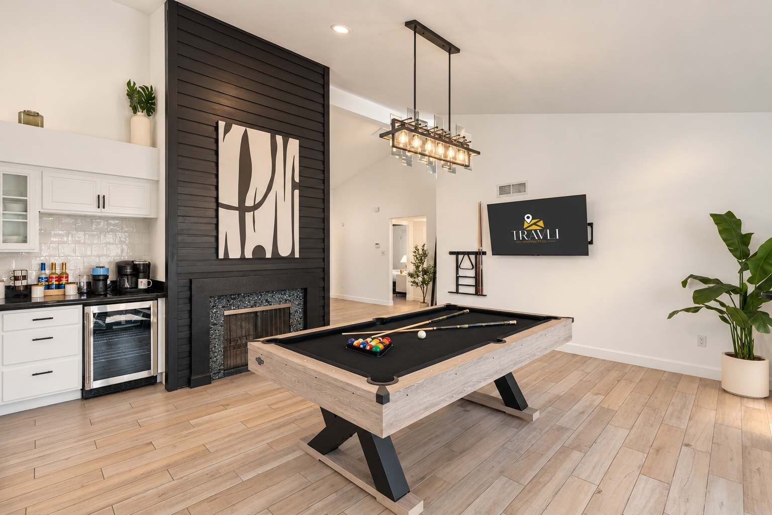 Una sala de estar moderna con mesa de billar, chimenea, zona de cocina y televisor montado.