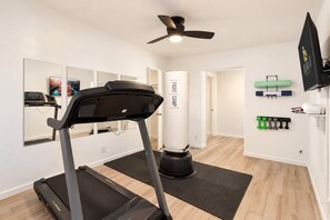Une salle de sport à domicile équipée d’un tapis de course, d’un sac de frappe et d’un téléviseur fixé au mur.