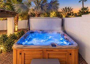 Un bain à remous avec un revêtement extérieur en bois, entouré d’un mur blanc et de palmiers.