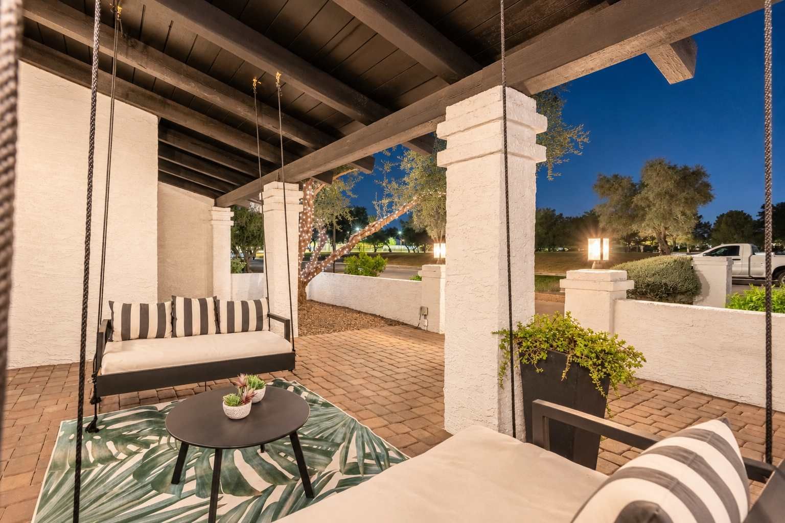 An outdoor patio with a swing chair, a round table, and a cushioned bench.