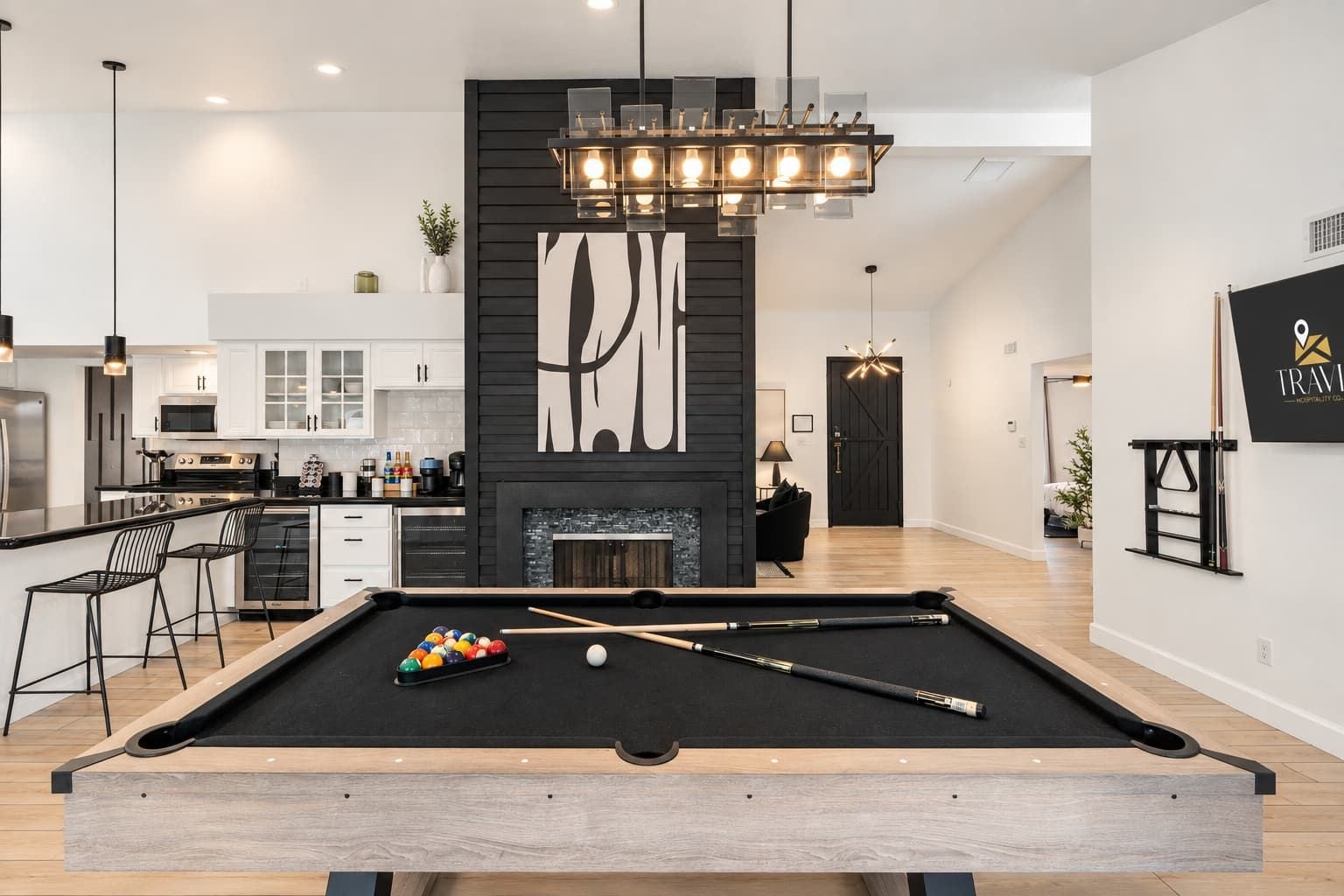 A modern living room with a pool table, a fireplace, and a kitchen area.