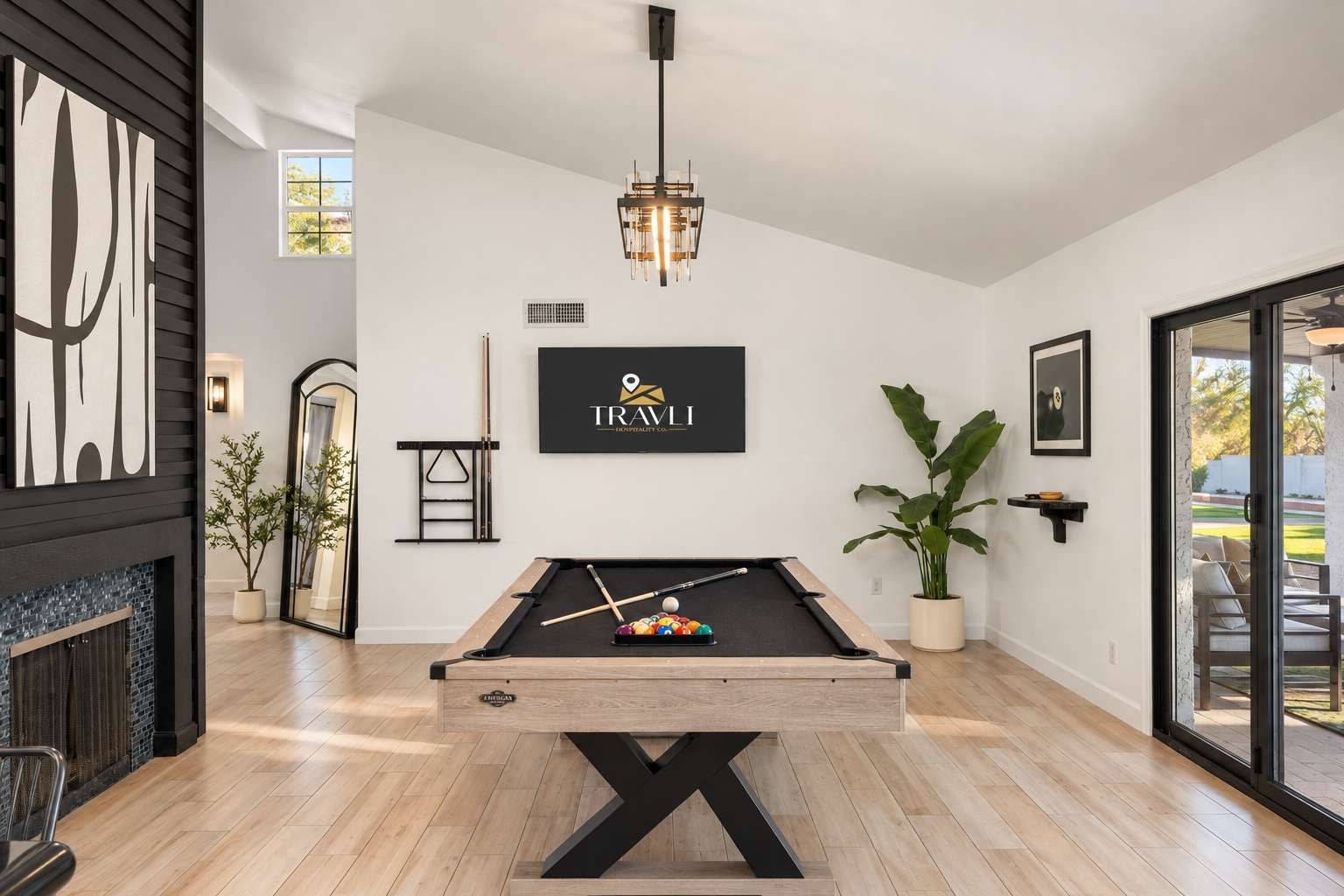 A pool table in a modern room with a fireplace, a framed logo on the wall, and a potted plant.