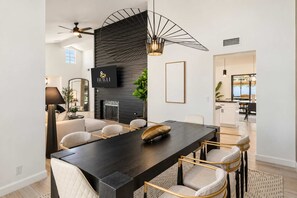 Un espace repas moderne avec une table en bois foncé, des chaises rembourrées, une cheminée et un téléviseur fixé au mur.