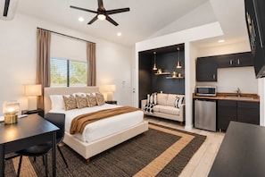 A modern hotel room with a bed, bedside table, lamp, and a view of the kitchen area. - Desert Playground |Pool|Sportcourt |Bocce | Cabana (Scottsdale)