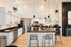 Une cuisine moderne avec des meubles blancs, des appareils en acier inoxydable et un îlot central doté de tabourets de bar.