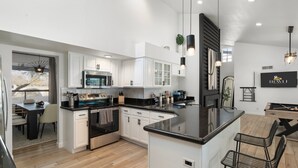 A modern kitchen with white cabinetry, a central island, and a dining area with bar stools. - Desert Playground | Pool, Gym, Bocce & Pickleball. (Scottsdale)
