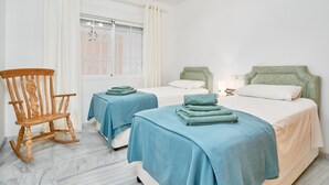 Une chambre avec deux lits, un fauteuil à bascule et une fenêtre avec des rideaux.
