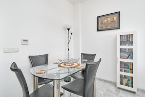 A modern dining area with a glass table, leather chairs, a decorative centerpiece, a floor lamp, a thermostat, and a bookshelf.