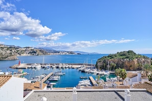 A marina with boats docked, a clear blue sky, and a mountainous backdrop.