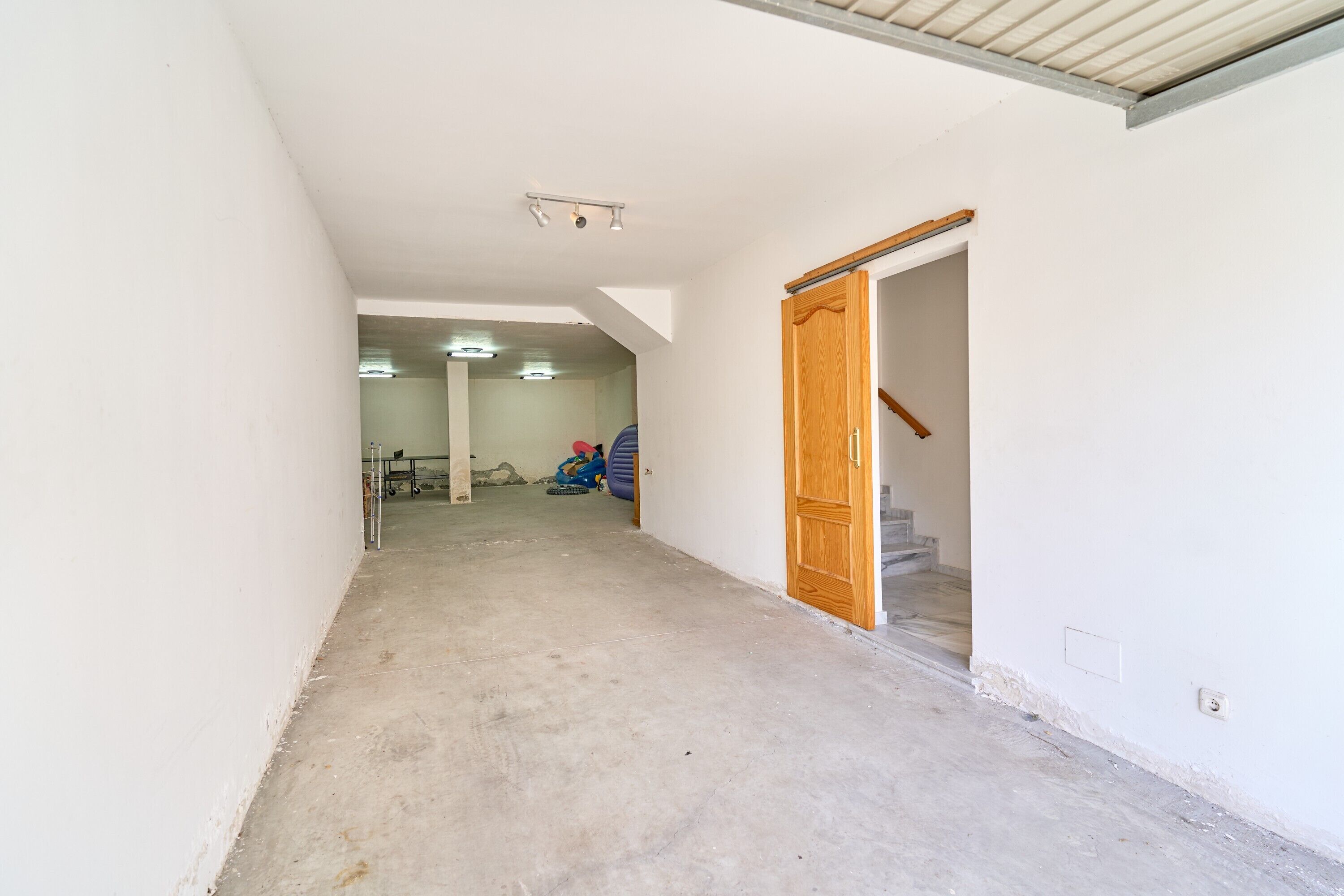 Ein Flur mit Holztür, Betonboden und einer Decke mit eingelassener Beleuchtung.