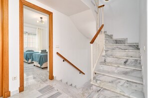 A marble staircase with wooden handrails, a wooden door frame, and a view into a room with a bed and a table.