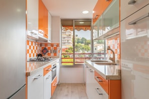 Una cocina compacta con electrodomésticos modernos, una ventana con vistas a edificios y un salpicadero de baldosas de cuadros.