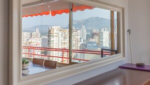 Una stanza con un'ampia finestra, un tavolo con sedie e vista su un paesaggio urbano con edifici e montagne.