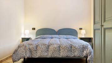 Un letto con copriletto a motivi floreali, due comodini con lampade e una porta a destra.