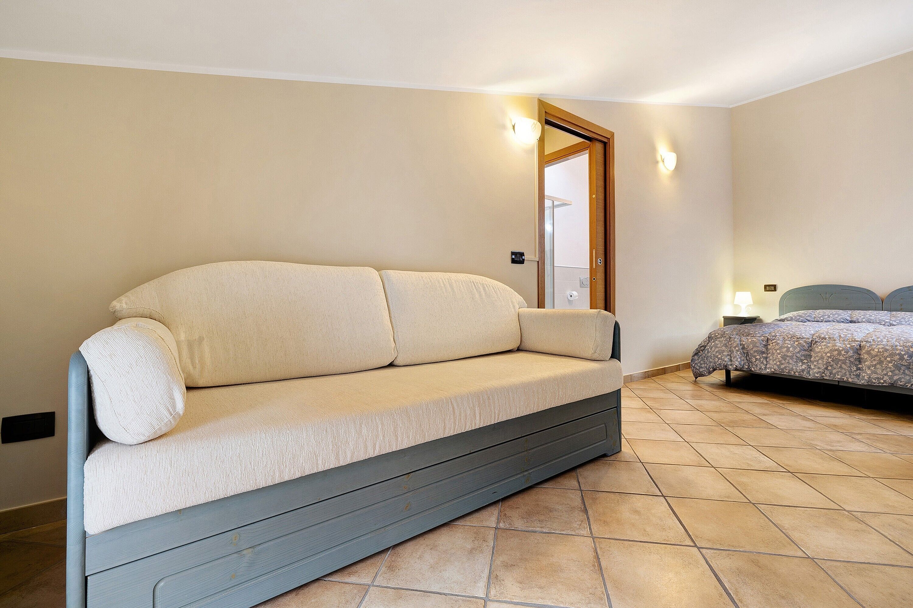 Ein Zimmer mit einer Couch, einem Bett, einer Tür und einer Wandleuchte.