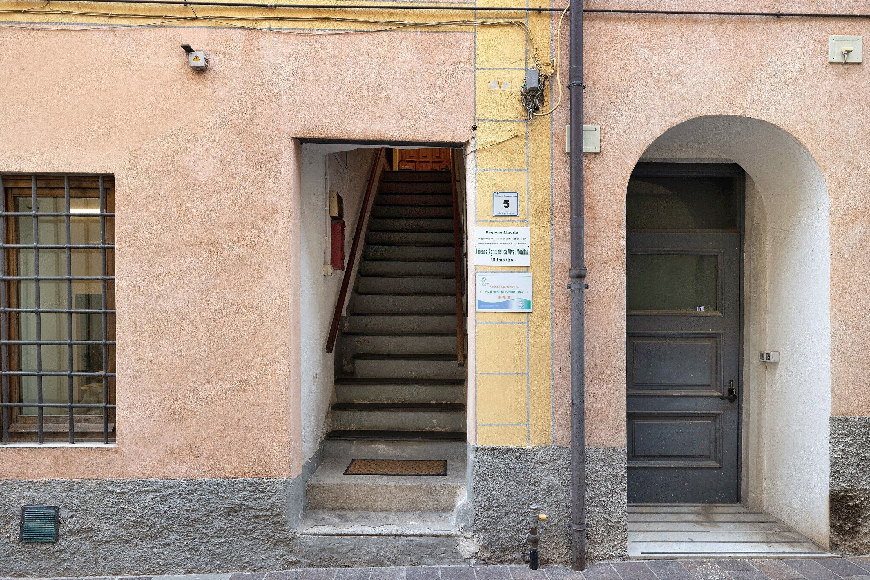 Un ingresso di un edificio con una scala che porta a una porta, una finestra con le sbarre e un cartello sul muro.