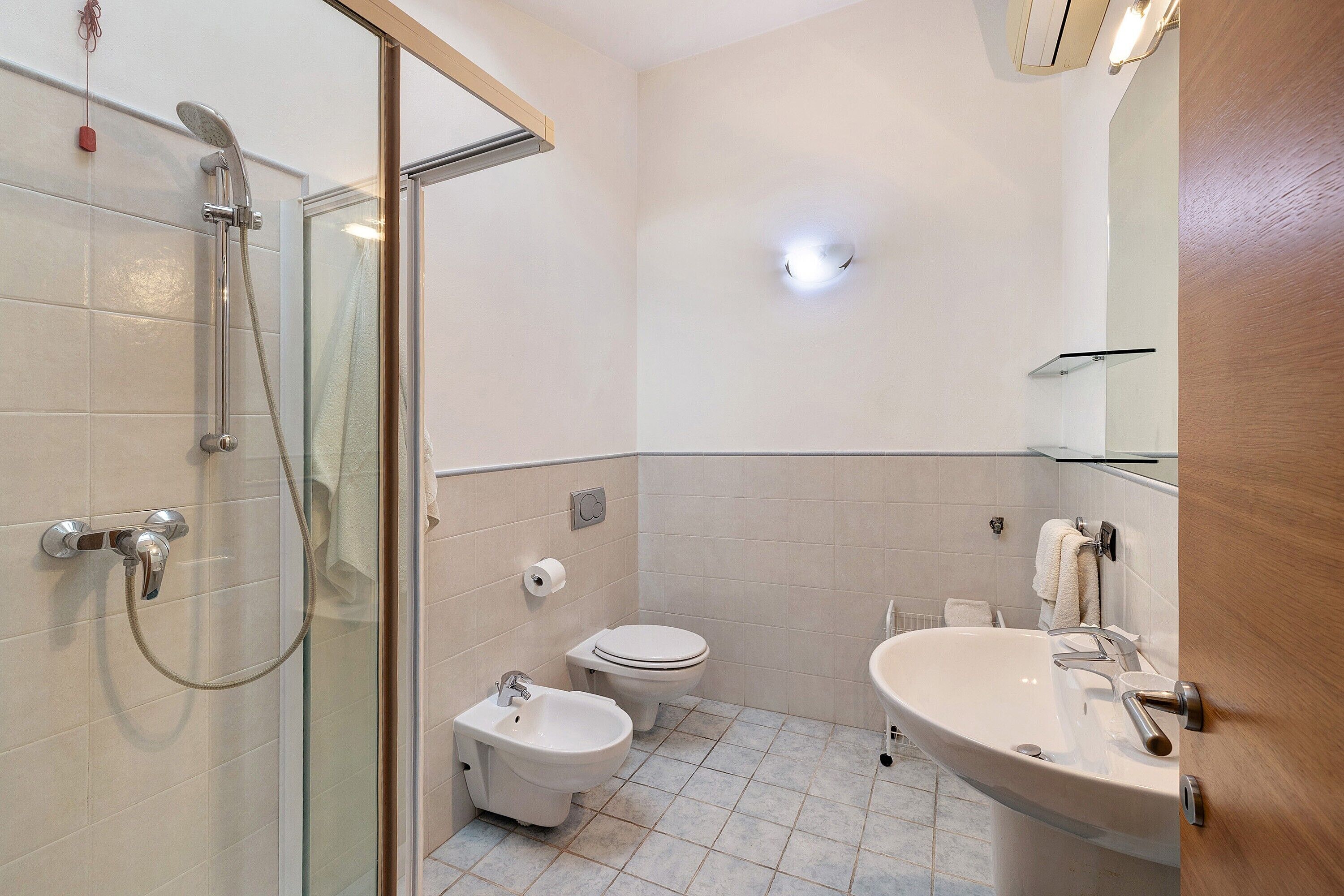 A bathroom with a glass shower enclosure, a bidet, a toilet, and a sink with a mirror.