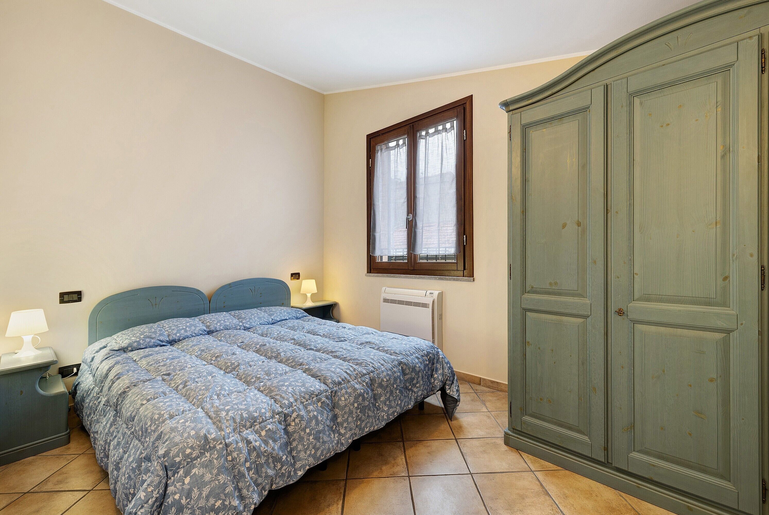 Une chambre à coucher comprenant un lit, une table de chevet, une commode, une fenêtre et un radiateur.
