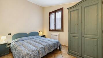 Une chambre à coucher comprenant un lit, une table de chevet, une commode, une fenêtre et un radiateur.