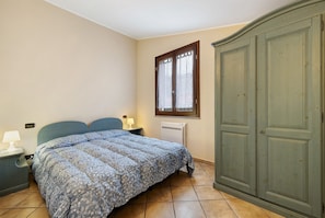 Un dormitorio con cama, mesita de noche, cómoda, ventana y radiador.