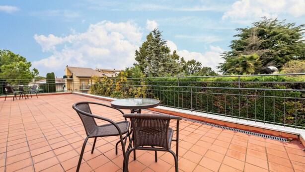 Una terraza con mesa y sillas, vistas al cielo y follaje circundante.